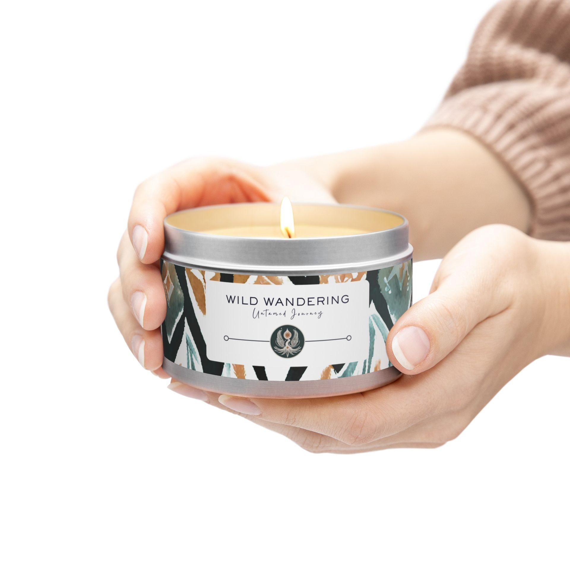 Person holding a lit Wild Wandering scented candle in a tin with a decorative label.