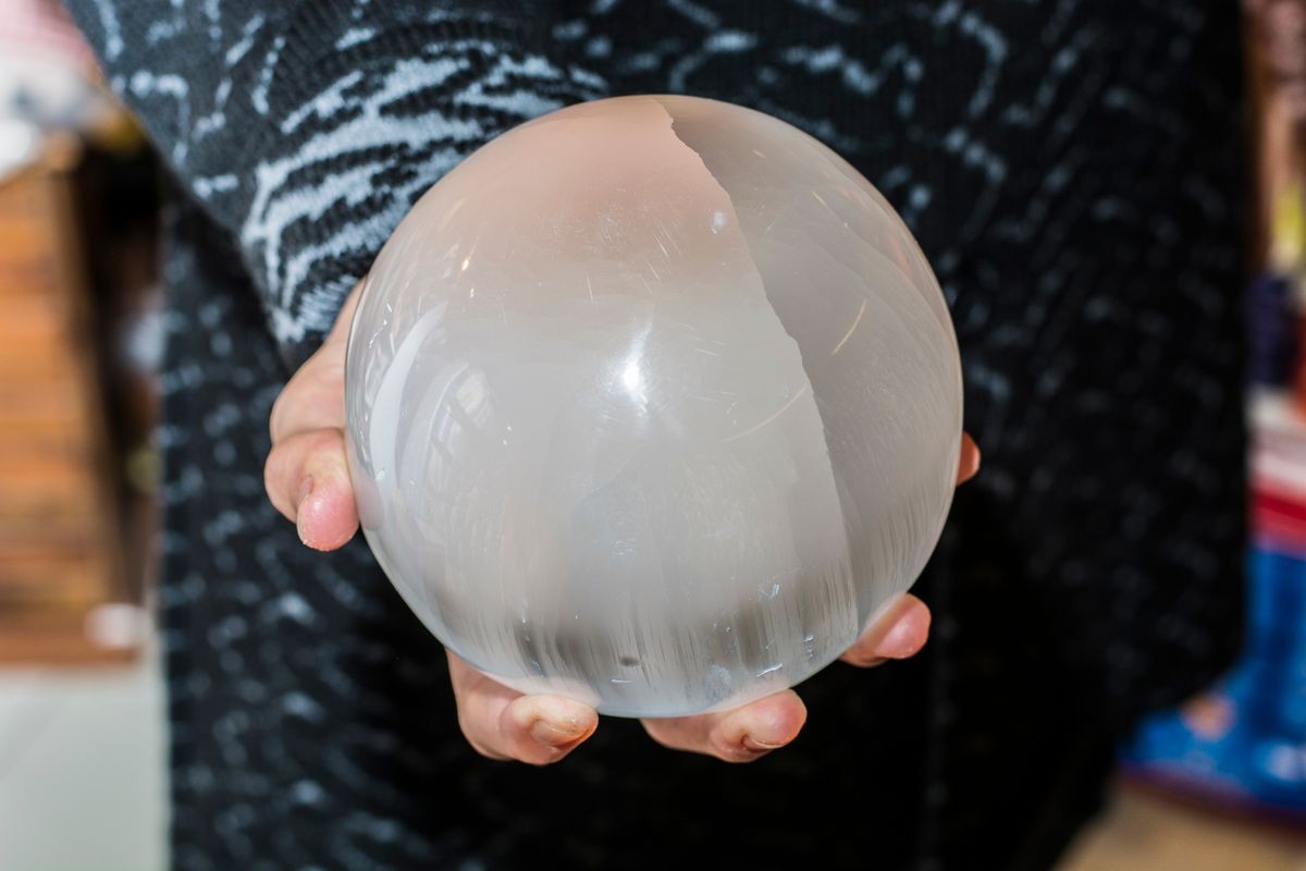 Close up shot of crop female hands holding sphere made of selenite or white quartz.